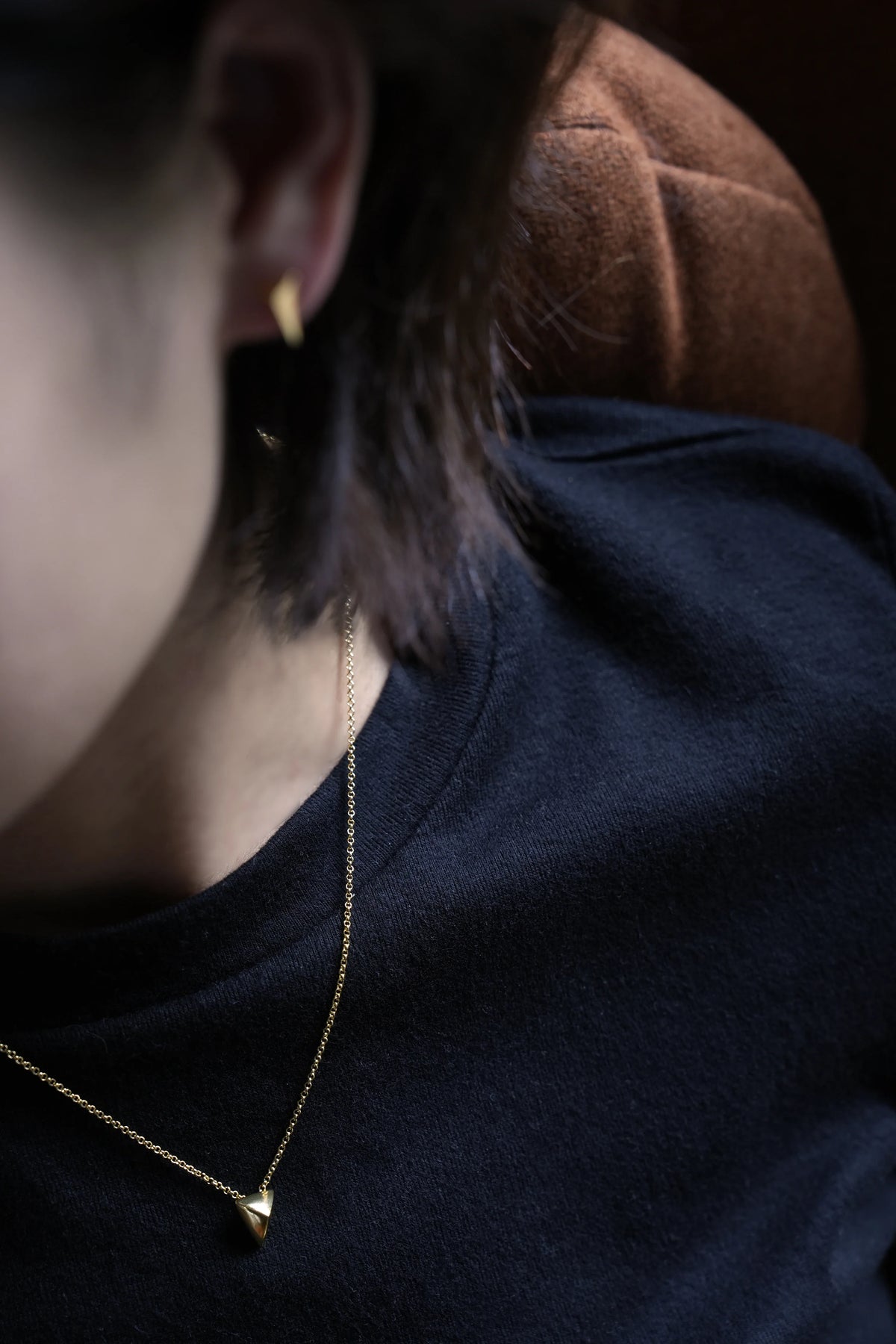 Close-up of a fine gold-tone chain necklace with a small triangle pendant worn over a dark T-shirt