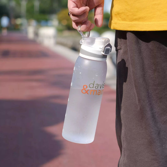 Hand carrying a frosted white water bottle with a Davis & Main print by its lid loop outdoors