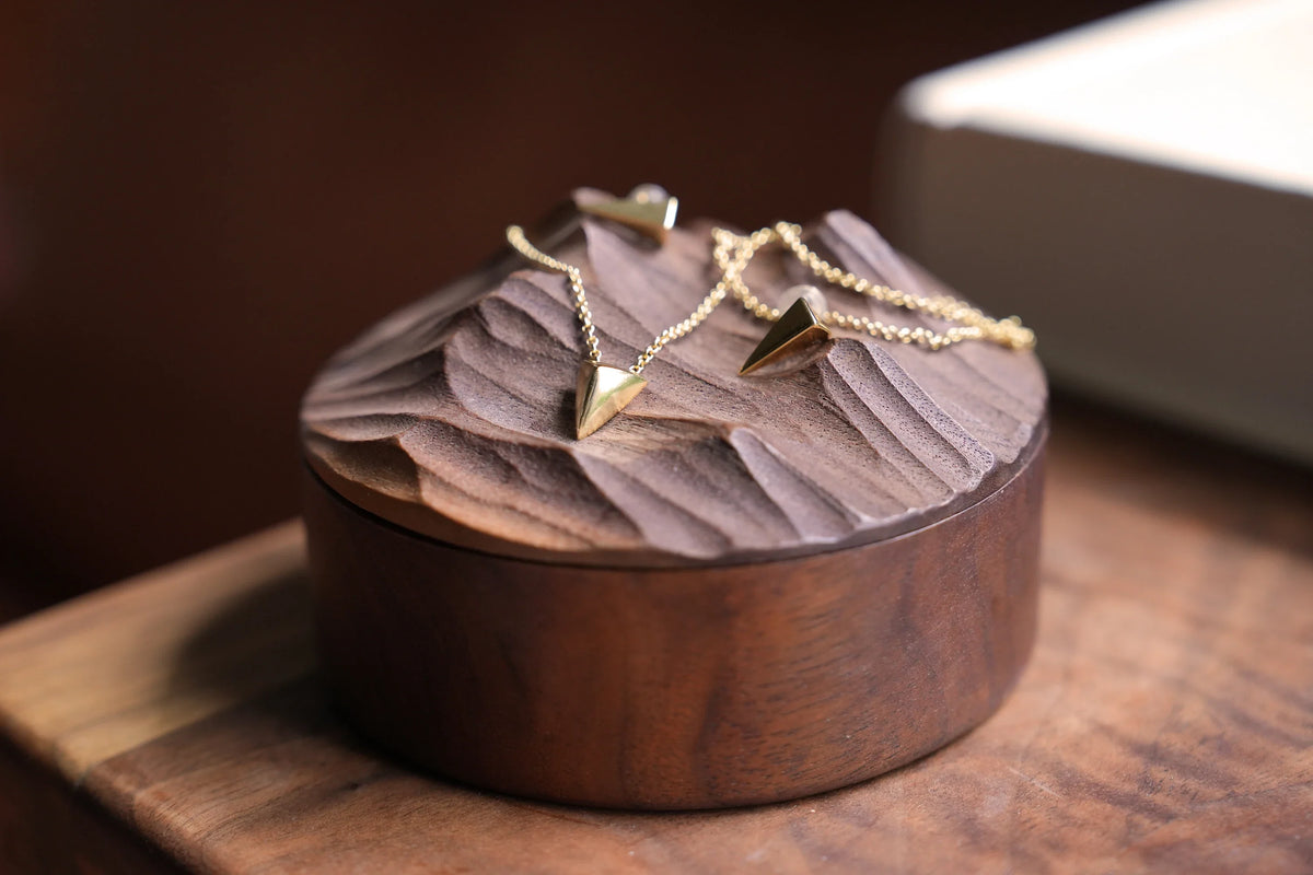 Gold-tone triangle pendant necklaces draped on a carved wooden jewelry box