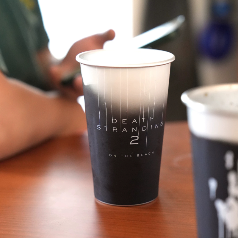 Tumbler fading from white at the rim to black, with white vertical line artwork, on a wooden table