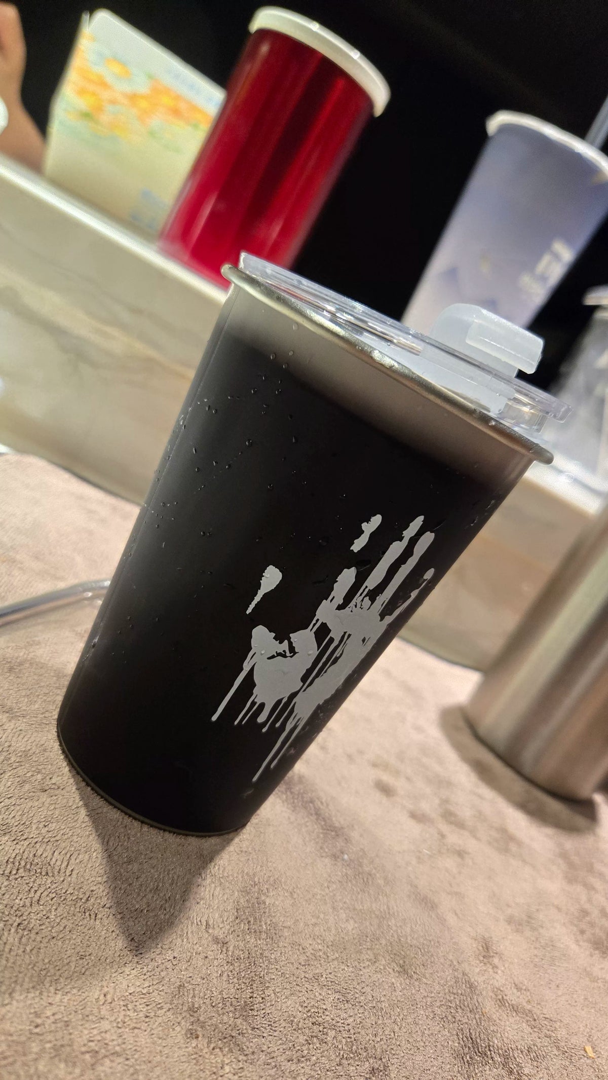 Black tumbler with a white handprint graphic and clear lid, beaded with condensation