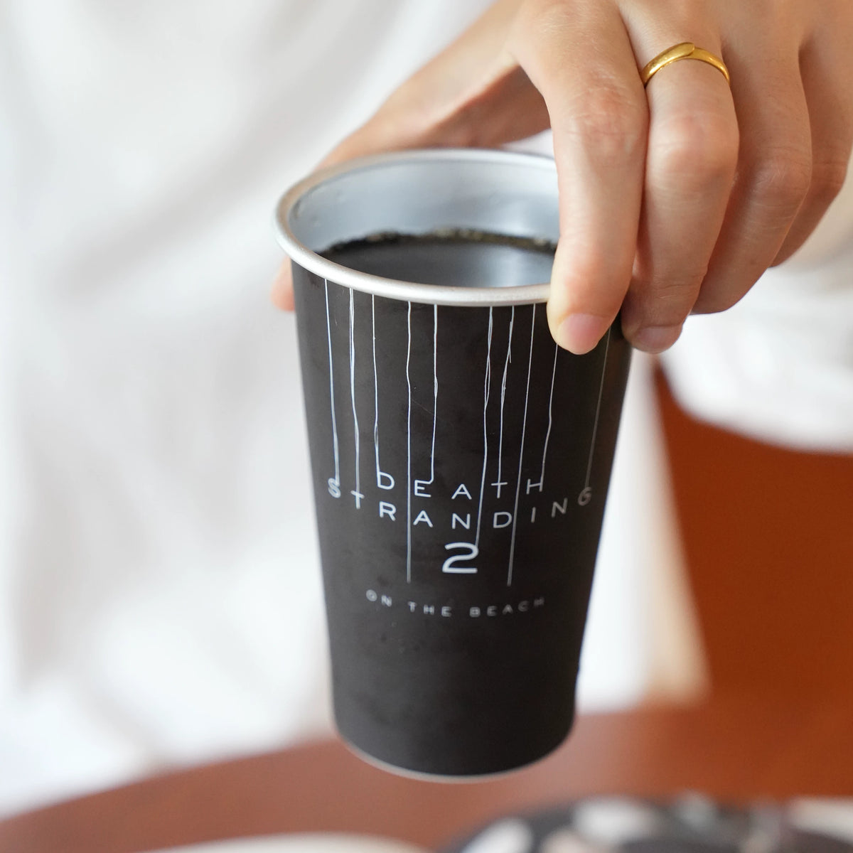 Hand holding a black metal tumbler with white vertical line artwork and printed title text